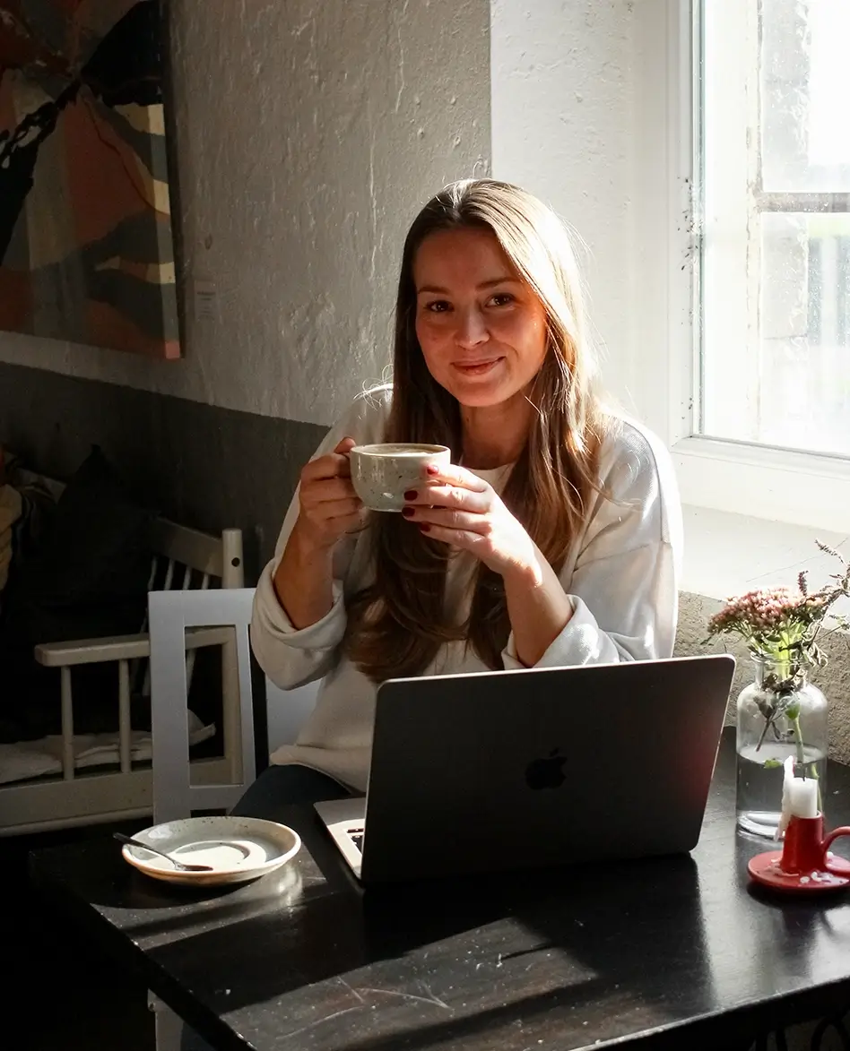 Grundare av Rosell Media tittar och ler mot kameran med en kaffe i handen framför en dator