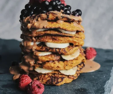 Veganska och glutenfria morotspannkakor toppade med jordnötssmör, bär och banan, ståendes på svart bricka och fotad av matfotograf Rosell Media